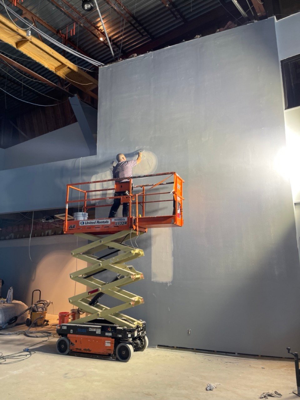 Commercial painting in Houston, TX with a painter rolling a high wall from a scissor lift